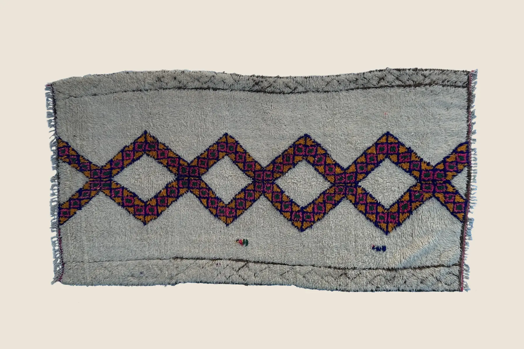 Beni M'Guild wool texture detail showing hand-knotted magenta and gold geometric motifs against forest green ground